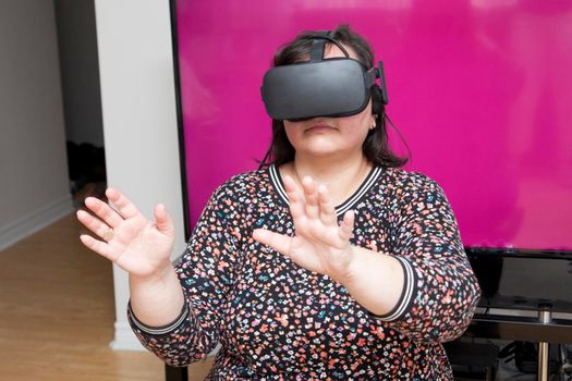 Woman in front of a television screen with blank space is playing a game using virtual reality headset