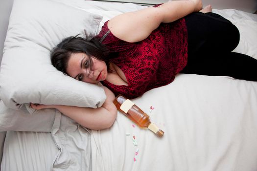 Woman sloppy or drunk in bed with a bottle and pills with copy space on bed 