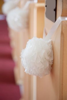 Wedding decoration in a church with a white hanging ball of flowers hung by a ribbon and blank pew plaque