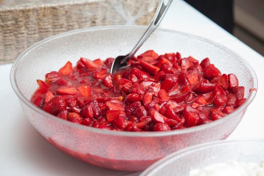 A large plastic dish of mashed strawberries with a spoon ready for dessert