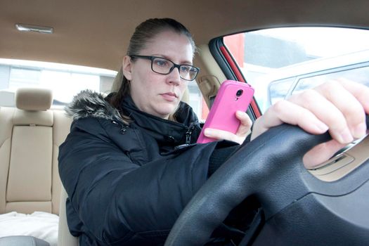 a woman looks at her cell phone while behind the wheel