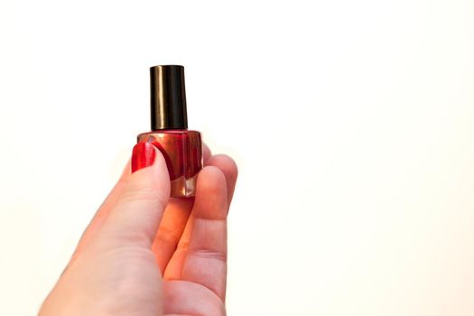 A hand holding a glass bottle with red shiny nail polish with a black cap against white copy space 