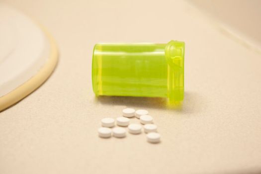 A handful of white pills on a counter in the bathroom with a bottle 