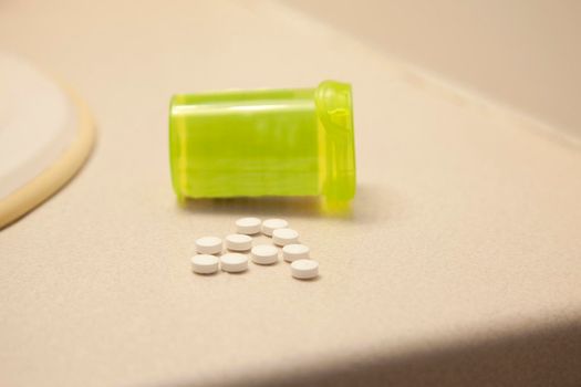 A green pill vial with white medication spilled onto the bathroom counter at home
