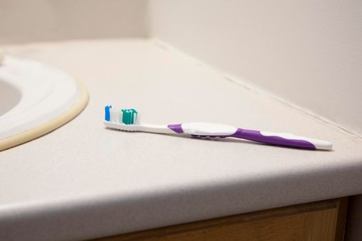 A purple and white toothbrush is on the bathroom counter at home