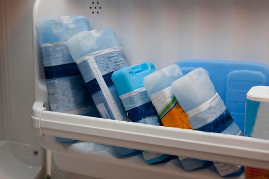 A row of blue cold packs frozen in the freezer shelf