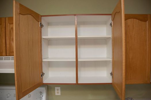 Kitchen cabinets with two wooden doors that are open showing empty shelves