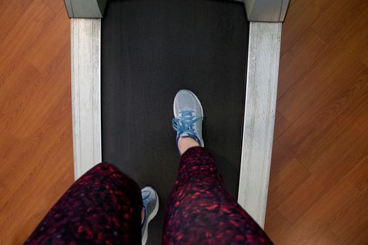  Looking down at a pair of legs and sneakers ready to run on a treadmill