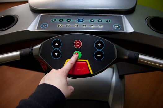 Get ready to run- hand pushes the green start button on a treadmill in a home gym 