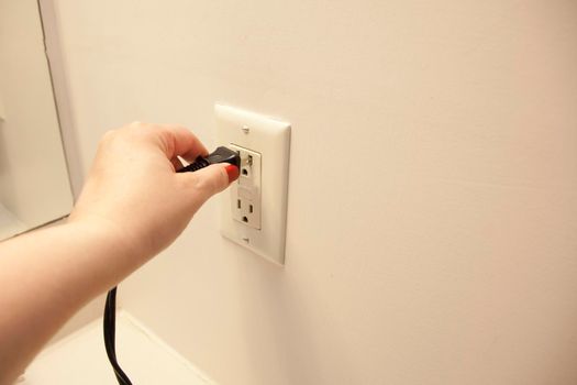 Hand plugs an electrical cord into an outlet at home