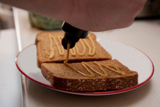 A person is pouring mustard onto their bread to make a sandwich