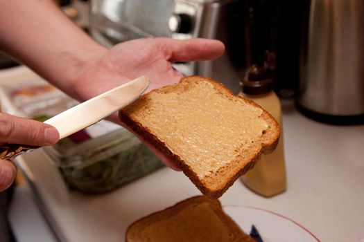  hand spreading mustard with a knife onto a piece of bread to make a sandwich