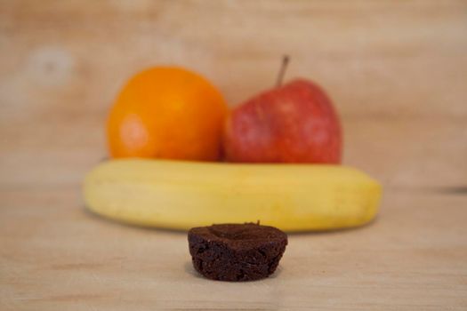 Fruits of apple, orange and banana with a small brownie in the foreground