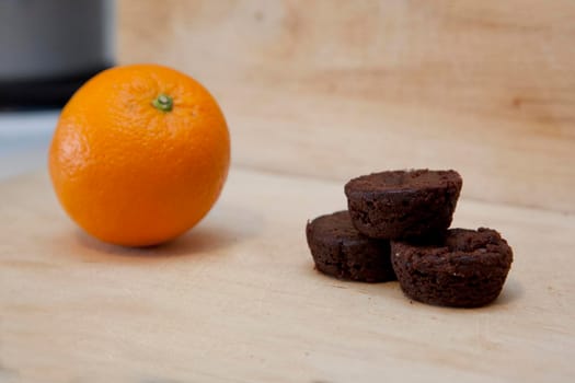 An orange and a small stack of brownies together on a kitchen cutting board