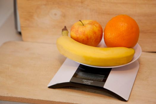 An apple, banana and orange on a digital scale to be weighed 