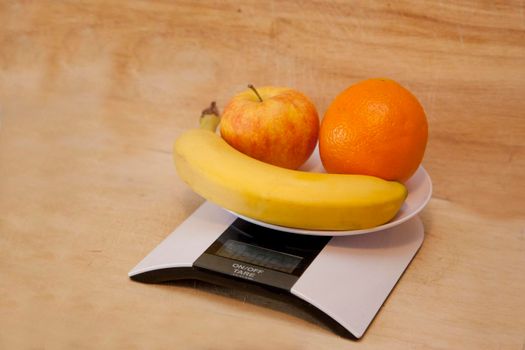 Banana, orange and apple on a digital scale being weighed as a healthy choice 