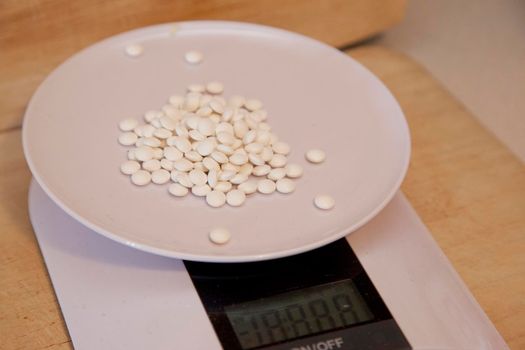 Dozens of tiny pills or vitamins on a kitchen scale being weighed