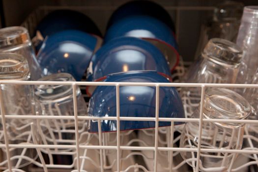 A top rack on a dishwasher with blue bowls and clear glasses 