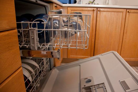 The top drawer of a dishwasher is full of bowls and glassware, in a home or apartment with wood cupboards 