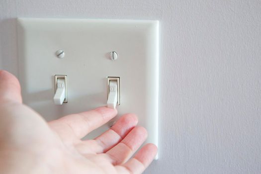 Hand about to turn a light switch from the off position to on 