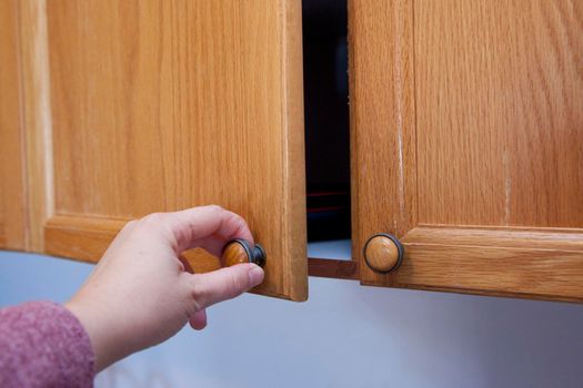  Hand pulling a wooden cupboard knob door to see what's inside 
