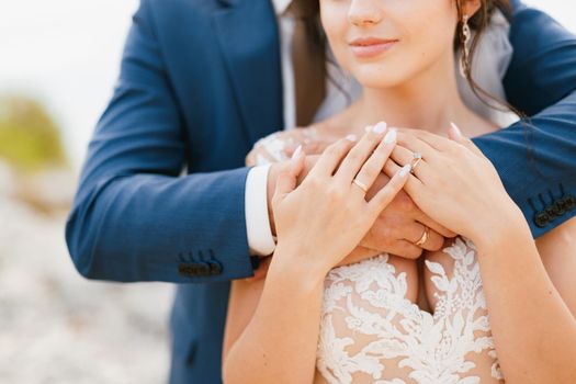 The groom gently hugs the bride by the shoulders, the bride put her hands on the groom's arms, close-up. High quality photo