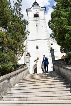 The Kiss. Bride and groom holding hands walking down the staircase in front of a small local church. Stylish wedding couple kissing.