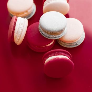 Pastry, bakery and branding concept - French macaroons on wine red background, parisian chic cafe dessert, sweet food and cake macaron for luxury confectionery brand, holiday backdrop design