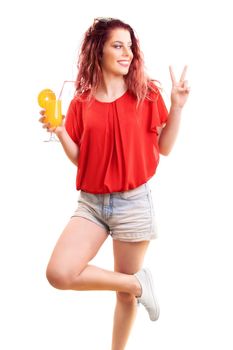 Portrait of a beautiful happy redhead young woman holding a cocktail or orange juice glass, showing the peace sign, isolated on white background. Summer time, cocktail, health concept.