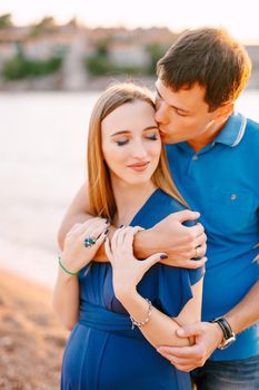 Man gently kisses smiling pregnant woman in a blue dress hugging her shoulders. High quality photo