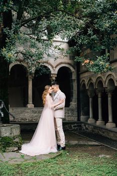 Groom hugs bride, standing in a green garden against the background of an old villa with columns on Lake Como, Italy. High quality photo