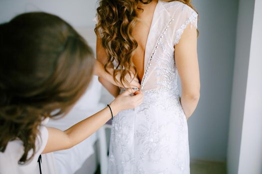 The bridesmaid helps the bride to button up the dress during the preparation for the wedding ceremony, back view . High quality photo