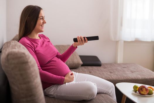 Happy pregnant woman enjoys watching tv and resting and her home.