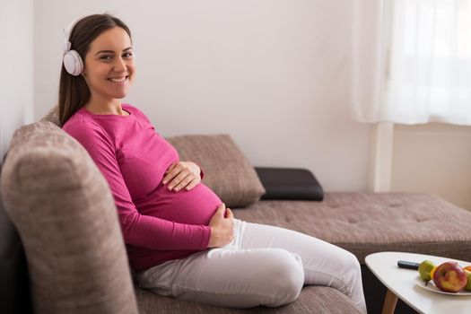 Beautiful pregnant woman enjoys listening  music at her home.