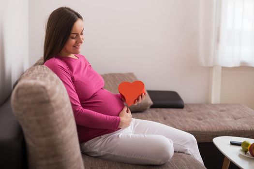 Happy pregnant woman  holding red heart shape.