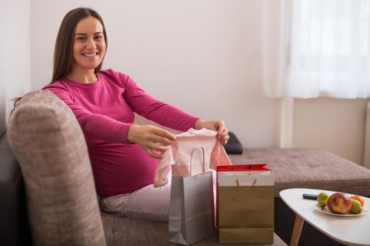 Happy pregnant woman with shopping bags and new baby clothes.
