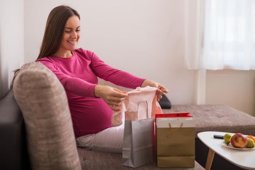 Happy pregnant woman with shopping bags and new baby clothes.