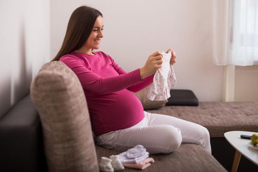 Happy pregnant woman holding baby clothes.