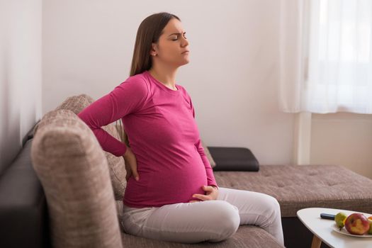 Pregnant woman having pain in back while spending time at her home.