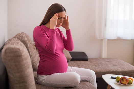 Pregnant woman having headache while spending time at her home.