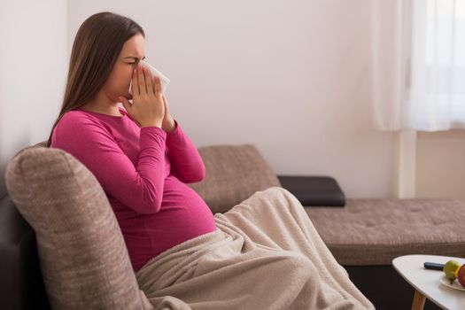 Exhausted pregnant woman having flu and blowing nose.