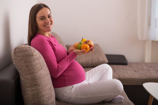 Happy pregnant woman holding bunch of fruit.