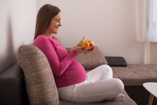 Happy pregnant woman holding bunch of fruit.