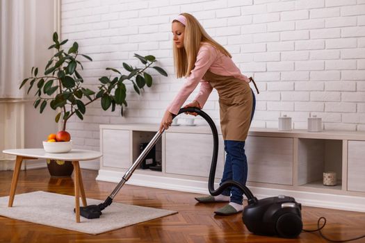 Beautiful housewife cleaning with vacuum cleaner her home.