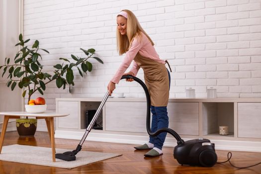 Beautiful housewife cleaning with vacuum cleaner her home.