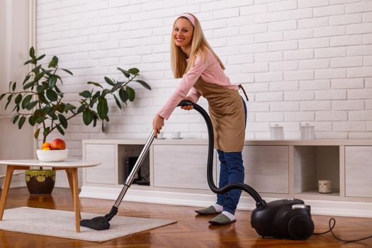 Beautiful housewife cleaning with vacuum cleaner her home.