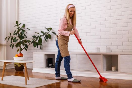 Beautiful housewife cleaning with broom her home.