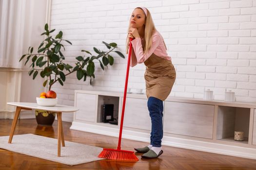 Tired housewife cleaning living room with a broom.