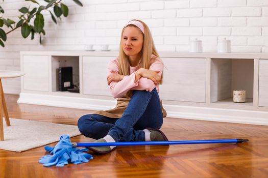 Image of angry and tired housewife with mop sitting  in the living room.
