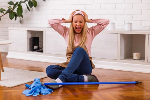 Image of  overworked housewife with mop shouting while sitting in the living room.